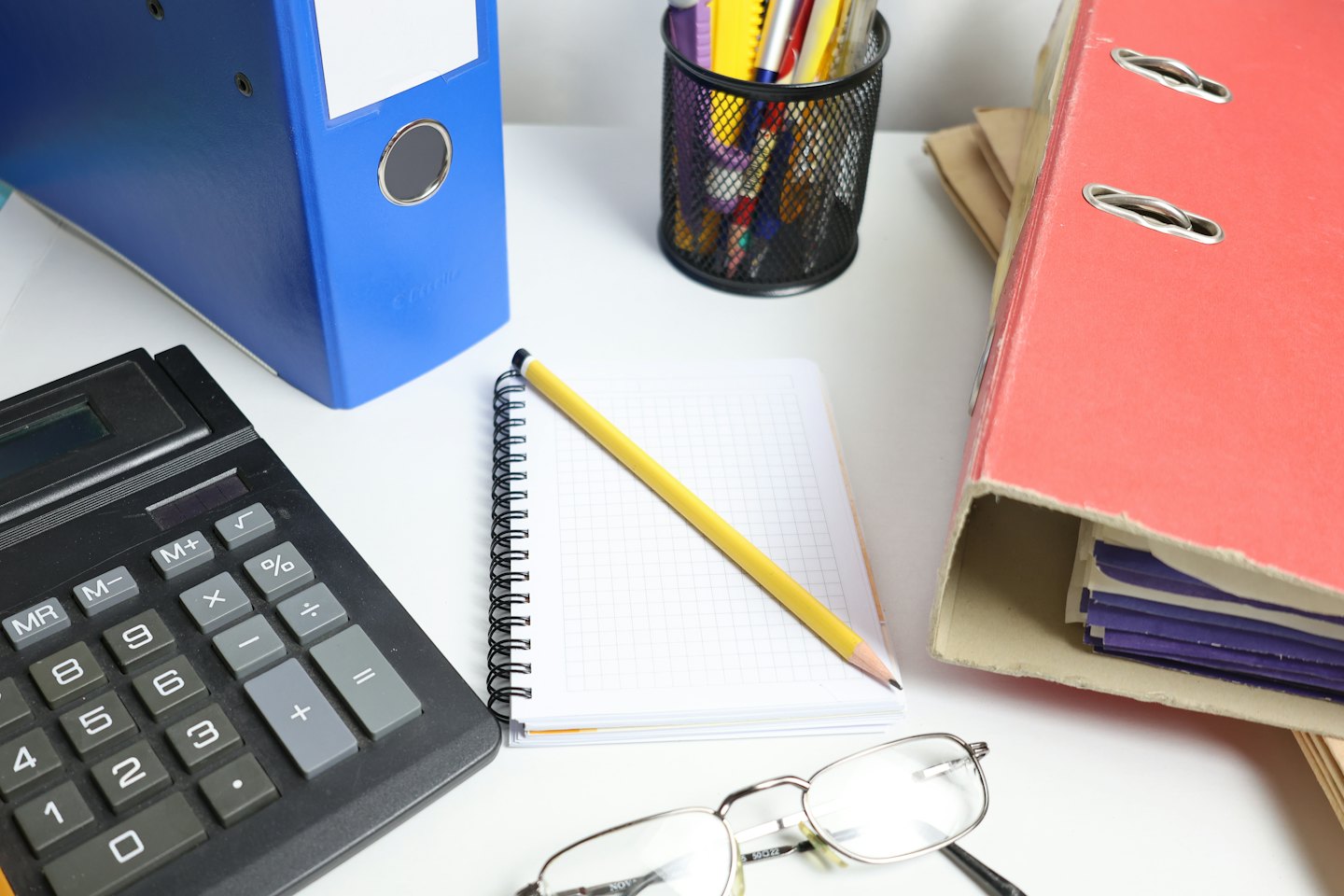 Escritorio de oficina con calculadora, carpetas, bloc de notas y gafas.