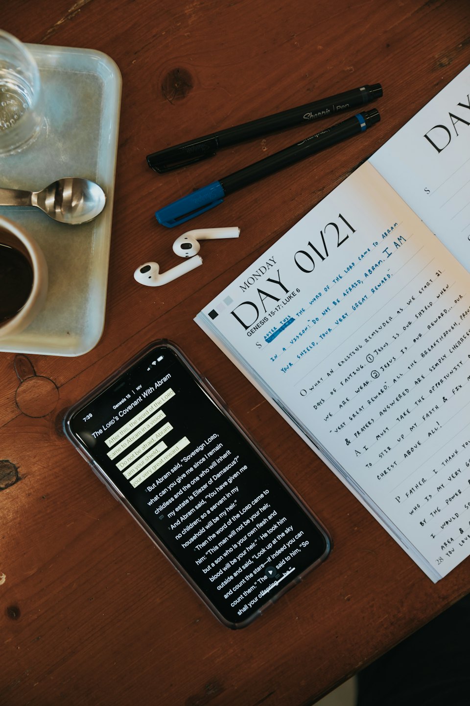 Un escritorio con una aplicación de la Biblia, agenda, café y agua.