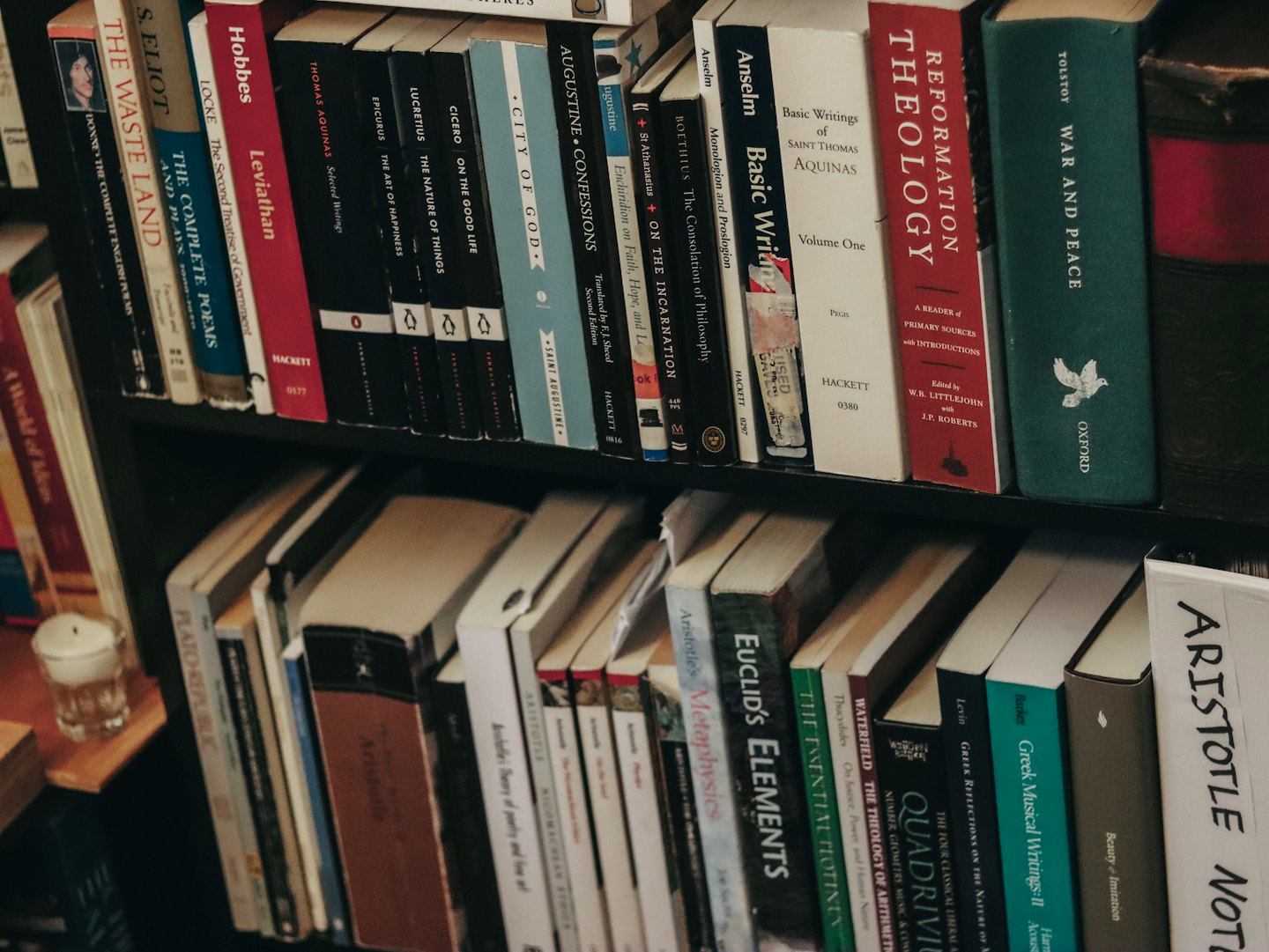 Dos estantes llenos de libros clásicos y una vela encendida.